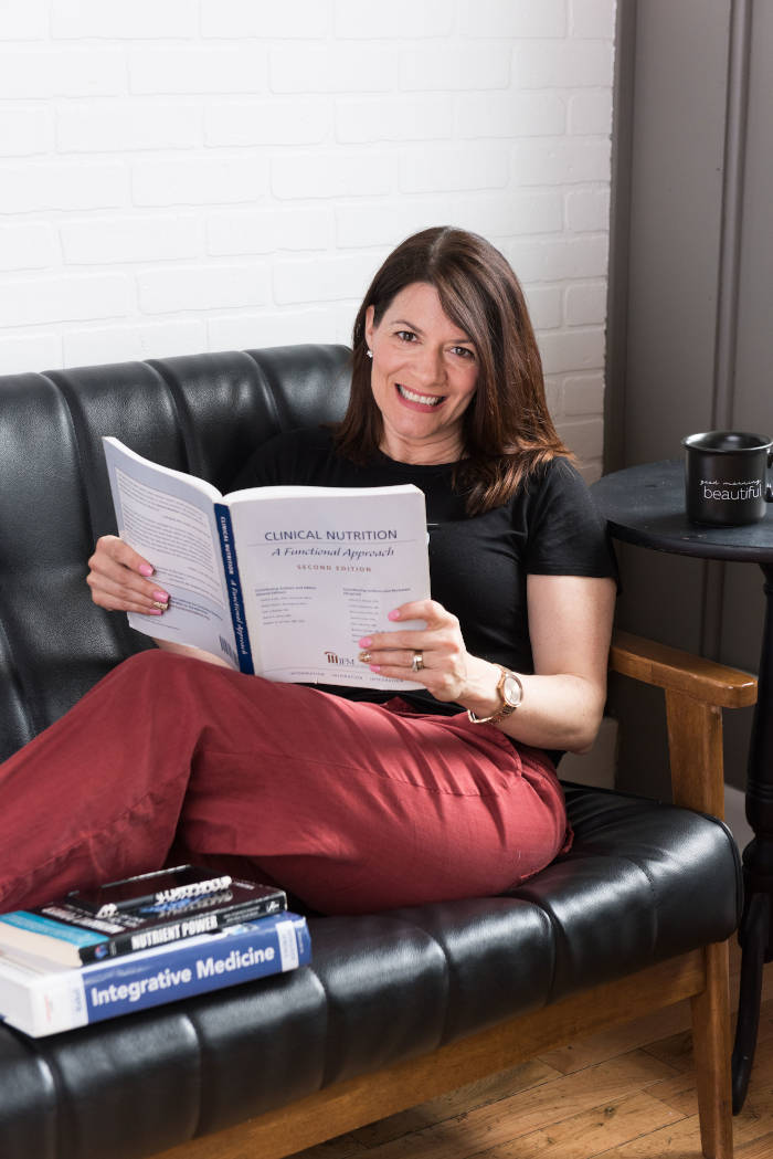 Amy Doyle sitting on couch reading functional nutrition books Amy Doyle sitting on couch reading functional nutrition books